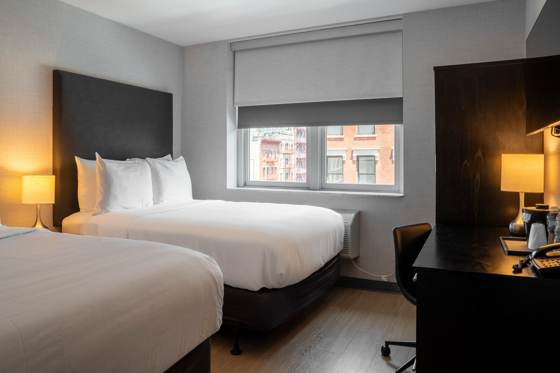 A hotel room with two beds, a desk, and a window.
