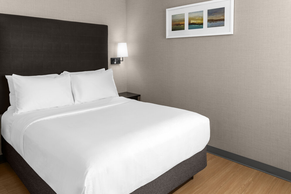 a bed with white sheets and a lamp on the wall